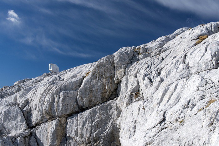 Ảnh chụp cận một dãy núi đá màu trắng, góc trên bên trái có một ngôi nhà nhỏ nhằm chênh vênh nhà nhỏ cheo leo trên vách núi