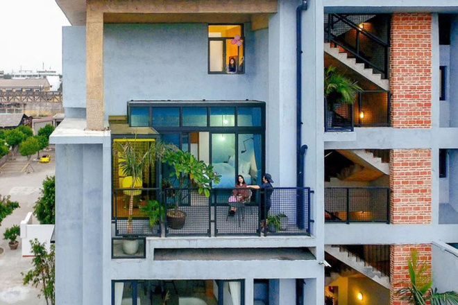 Ảnh chụp cận phía mặt tiền ở giữa nhà, trên ban công có hai người một ngồi, một đứng, tầng trên có một người đứng ở cửa sổ ban công ngắm cảnh ban công nhà đẹp