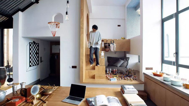 Cận cảnh căn phòng nhỏ có khung cửa kính bên phải, góc trong cùng bên phải là giường ngủ đặt trên bục cao, một người đàn ông đang bước xuống trên bậc thang, cận cảnh là phản ngồi làm việc và những đồ trang trí nhỏ thiết kế nhà độc đáo