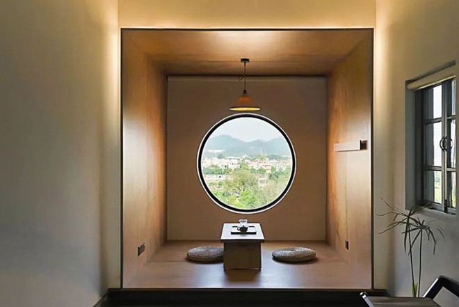 Cận cảnh một phòng trà hình hộp, có một phản gỗ bày bàn nhỏ và nệm ngồi, chình giữa là một ô cửa hình tròn nhìn ra bên ngoài phòng trà