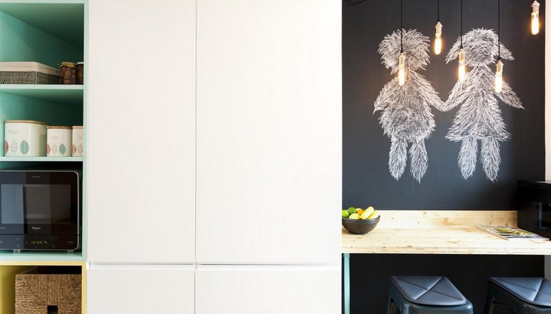 Bên trái là tủ lưu trữ nhiều ngăn, bên phải là góc ăn sáng gồm hai ghế đơn, tường sơn đen và đèn thả góc ăn sáng