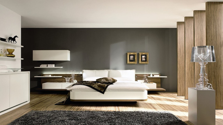 Ảnh chụp phòng ngủ của bố mẹ thoáng, sáng nhờ thiết kế hệ cửa sổ kính lớn. Mảng tường xám đầu giường giúp làm nổi bật chiếc giường với ga, gối màu trắng cũng hệ kệ lưu trữ sáng màu. Phòng ngủ của bố mẹ