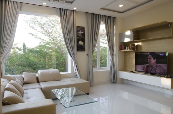 Ảnh chụp không gian sinh hoạt chung của gia đình ở tầng trên với bộ sô pha lớn màu da, ti vi treo tường và hệ cửa sổ kính lớn, giúp mở rộng tầm nhìn ra ngoài thiết kế nhà phố tràn ngập ánh sáng