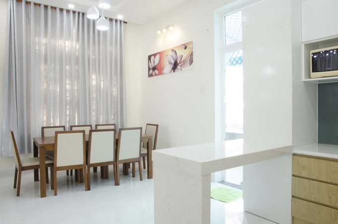 Trong ảnh là khu vực bếp - ăn, được ngăn cách bởi đảo bếp trắng với bộ bàn ăn đơn giản, gồm 8 ghế ngồi thiết kế nhà phố 4 tầng tràn ngập ánh sáng