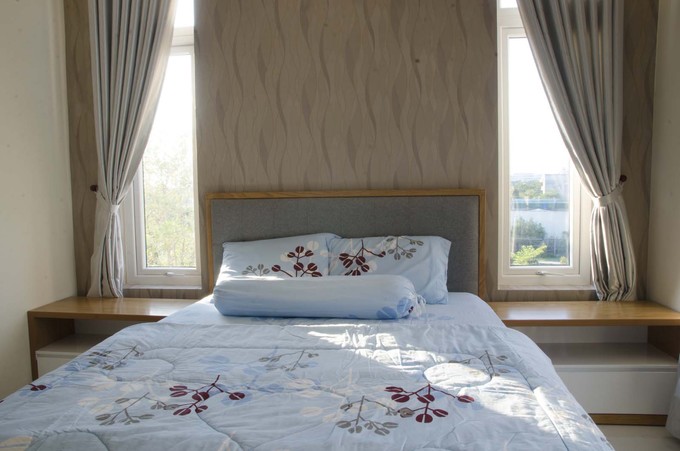 Ảnh chụp phòng ngủ của con với chiếc giường lớn, được trải ga màu xanh nhạt và thiết kế hệ kệ lưu trữ bằng gỗ nơi đầu giường phòng ngủ trong ngôi nhà Sài Gòn